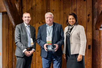 Three professionally dressed people, one holding award plaque.