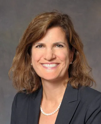 Professional woman smiling, wearing blazer and pearls.