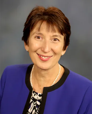 Professional woman smiling, wearing blue blazer and pearl necklace